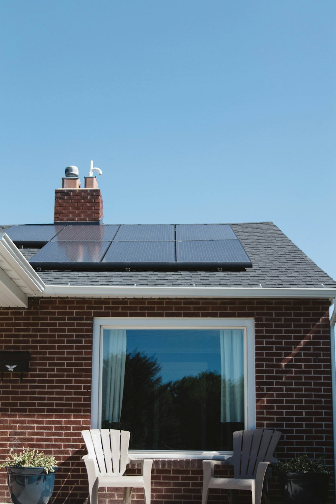 about-us Vivint Solar - Solar Panels on roof of brick home with window and Adirondack chairs.